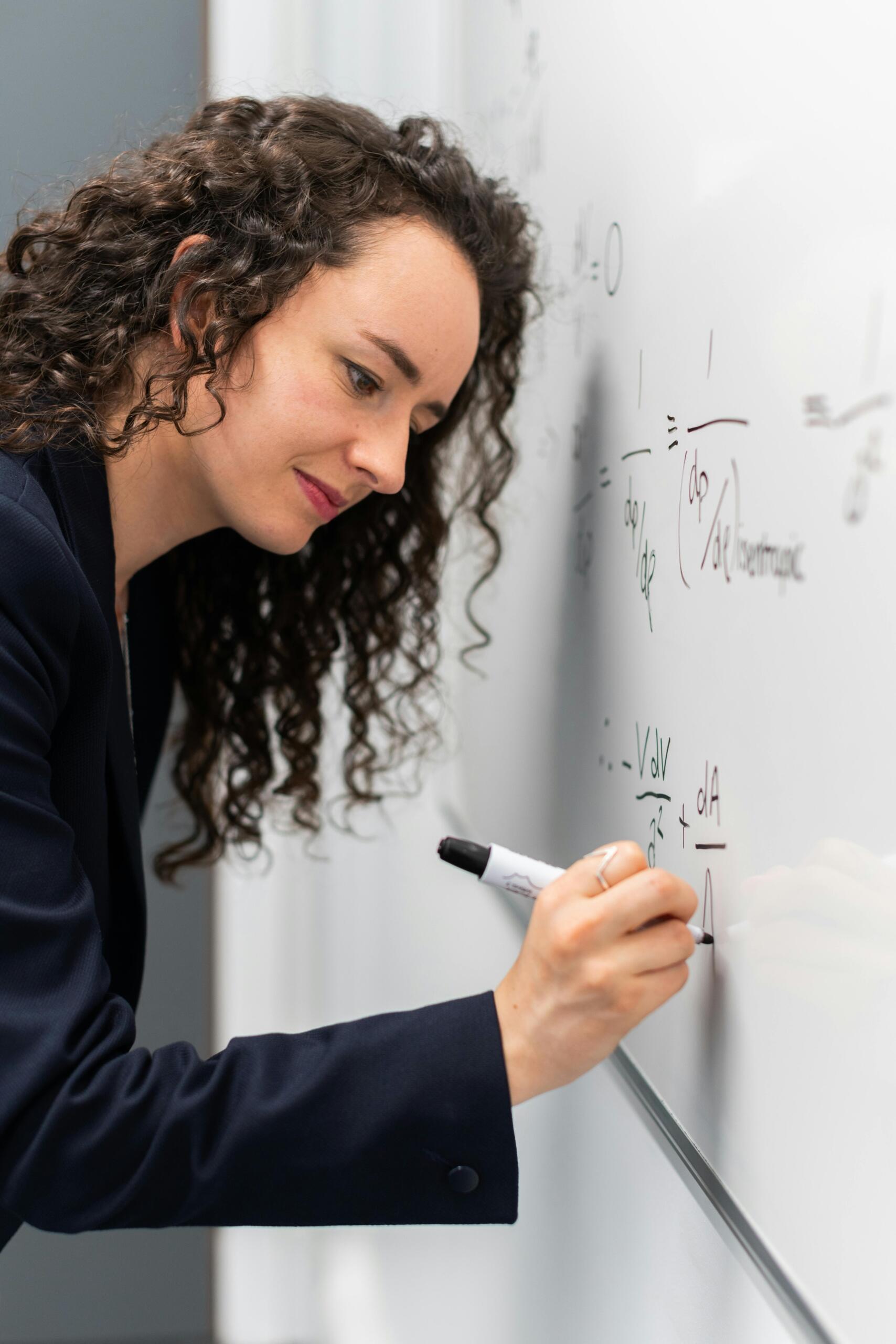 Woman writing a mathematical formula on a whiteboard.