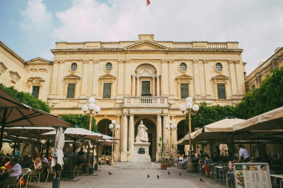 Outdoor cafés and people in front of the National Library of Malta in Valletta.