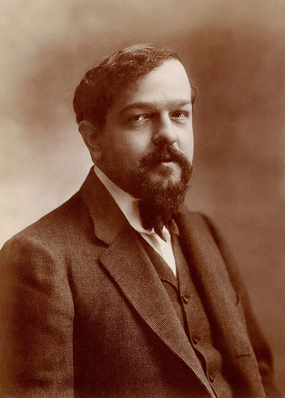Sepia-toned portrait of Claude Debussy featuring a full beard, dark suit jacket, vest, and a slightly upward gaze.